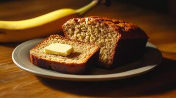 Freshly baked banana bread with butter on a plate beside a ripe banana in warm lighting photo