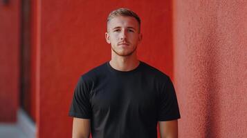 Young man standing confidently against a vibrant red wall in an urban setting during daylight photo