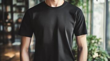 A man showcases a plain black t-shirt in a modern indoor setting with greenery and natural light photo