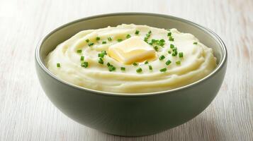 Creamy mashed potatoes topped with butter and chives served in a green bowl on a wooden table photo