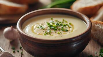 Creamy potato soup garnished with fresh herbs served in a rustic bowl with slices of bread nearby on a wooden table photo