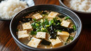 Tofu soup with green onions and seaweed served alongside bowls of rice on a wooden table photo