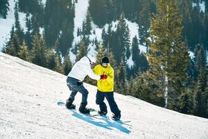 Goderdzi, Georgia - 13 th january, 2023 - male hipster instructor hold hands show how to snowboard keep balance beginner snowboarder downhill on white slope in ski resort. Lessons learn to ski photo