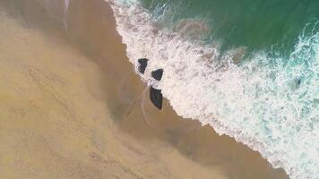 aerial with drone, static shot over the shore of a beach, footage of the the waves breaking against an isolated rock video