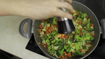 Adding salt to fresh vegetables on frying pan. Carrots, cauliflower, broccoli video
