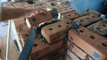 Masonry Work with Bricks and Mortar. A close-up view of a bricklaying process, where a construction worker is applying mortar to bricks. video