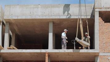 Construction Workers Managing Concrete Slab Placement. Two construction workers are overseeing the placement of a concrete slab on an upper level of a building under construction. video