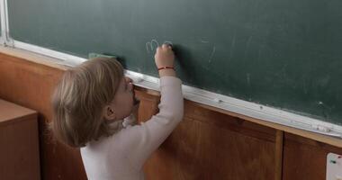 Girl drawing at blackboard using a chalk in classroom. Education process video