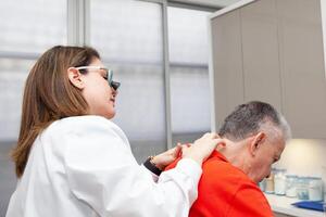 Dermatologist making a routine checkup on a senior male patient using a binocular loupe. photo