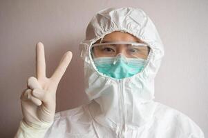 Nurse wearing PPE suit with mask for protect virus and showing victory. In coronavirus pandemic outbreak we should support and encourage healthcare worker by stay home and listen to medical advice. photo
