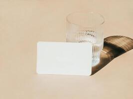 White blank card for text mockup and glass of water on beige background. photo