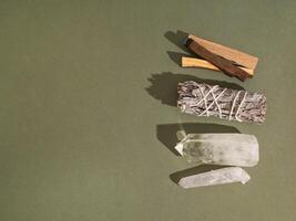 Items for spiritual cleansing - sage bundle, palo santo incense sticks and quartz crystal on green background. photo