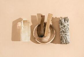 Collection items for spiritual cleansing - sage bundle, palo santo incense sticks and quartz crystal on beige background. photo