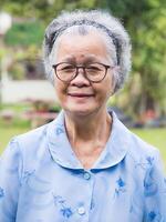 Portrait of a senior woman with short gray hair, wearing glasses, and looking at the camera with a smile while standing in a garden. Aged people and relaxation concept photo