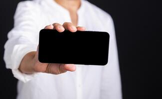 Close-up of hand holding a smartphone while standing in the studio with a black background. Close-up photo. Space for text. Technology, communication concept photo