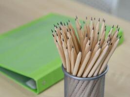 Many pencils are in the mesh box on a wooden table. Space for text. Close-up photo
