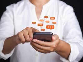 Businesswoman using a smartphone with a conversation icon while standing with a gray background. Space for text. Communication and technology concept photo
