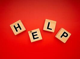 HELP word is written on wood blocks isolated on a red background. Top view. Close-up photo