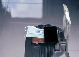 A smartphone on mask and passport placed on suitcase. Space for text. Technology, journey and healthcare concept photo