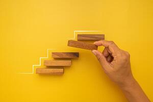 Hand of holding empty wooden blocks arranging to stack as step stair isolated on yellow background. Business growth and success process concept photo