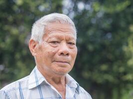 Portrait of a senior man with short gray hair smiling and looking at the camera while standing in a garden. Aged people and healthcare concept photo
