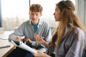 students sit at shared desk making notes studying together at university photo