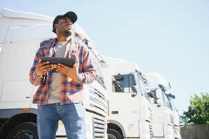 African American professional truck driver setting up navigation for destination. Checking his route on tablet computer and standing by long vehicle. Transportation service photo