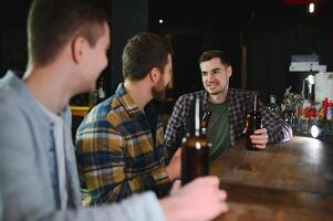 Young men in casual clothes are talking, laughing and drinking while sitting at bar counter in pub photo