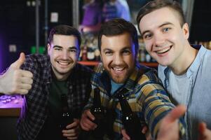 Young men in casual clothes are talking, laughing and drinking while sitting at bar counter in pub photo