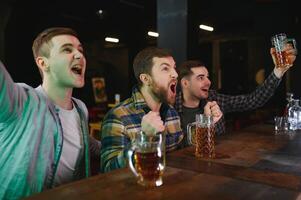 Soccer fans cheering for favourite team while enjoying drinks. Group of supporters celebrating victory while watching football match on tv in a club. Happy friends shouting while cheering for a goal. photo