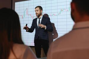 Man is standing near projector and showing graphs and business graphs. photo