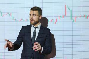Man is standing near projector and showing graphs and business graphs. photo