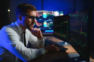 Side view of crypto broker sitting at office table, analyzing market, looking at screen photo