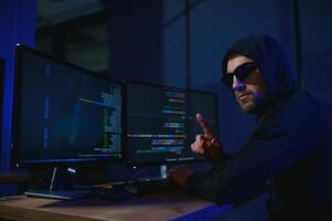 hacker sitting at desk in dark atmosphere. A computer programmer or hacker. Anonymous computer hacker. photo