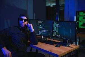 hacker sitting at desk in dark atmosphere. A computer programmer or hacker. Anonymous computer hacker. photo