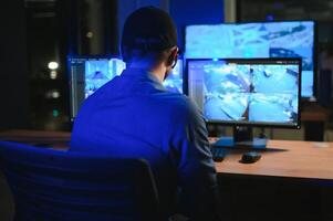 Rear view of security system operator looking at CCTV footage at desk in office photo