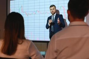 Man is standing near projector and showing graphs and business graphs. photo