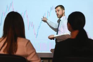 Man is standing near projector and showing graphs and business graphs. photo