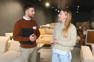 Smiling female customer looking while listening to employee discussing about sofa at store photo