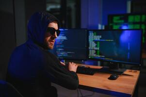 hacker sitting at desk in dark atmosphere. A computer programmer or hacker. Anonymous computer hacker. photo