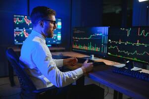 Side view of crypto broker sitting at office table, analyzing market, looking at screen photo