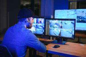 Rear view of security system operator looking at CCTV footage at desk in office photo