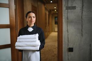 The maid is standing in the corridor of the hotel and holding clean towels photo