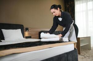 Housemaid making bed in hotel room while folding towels photo