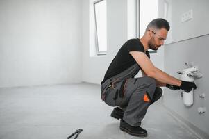 Young man in workwear using pliers while installing water filtration system photo