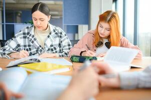 students sit at shared desk making notes studying together at university photo