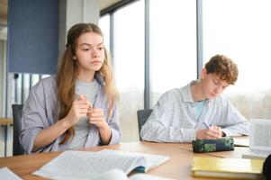 students sit at shared desk making notes studying together at university photo
