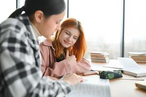 students sit at shared desk making notes studying together at university photo