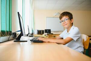Teenage boy smiling while using computer at desk in classroom photo