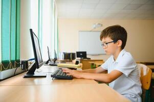 Teenage boy smiling while using computer at desk in classroom photo